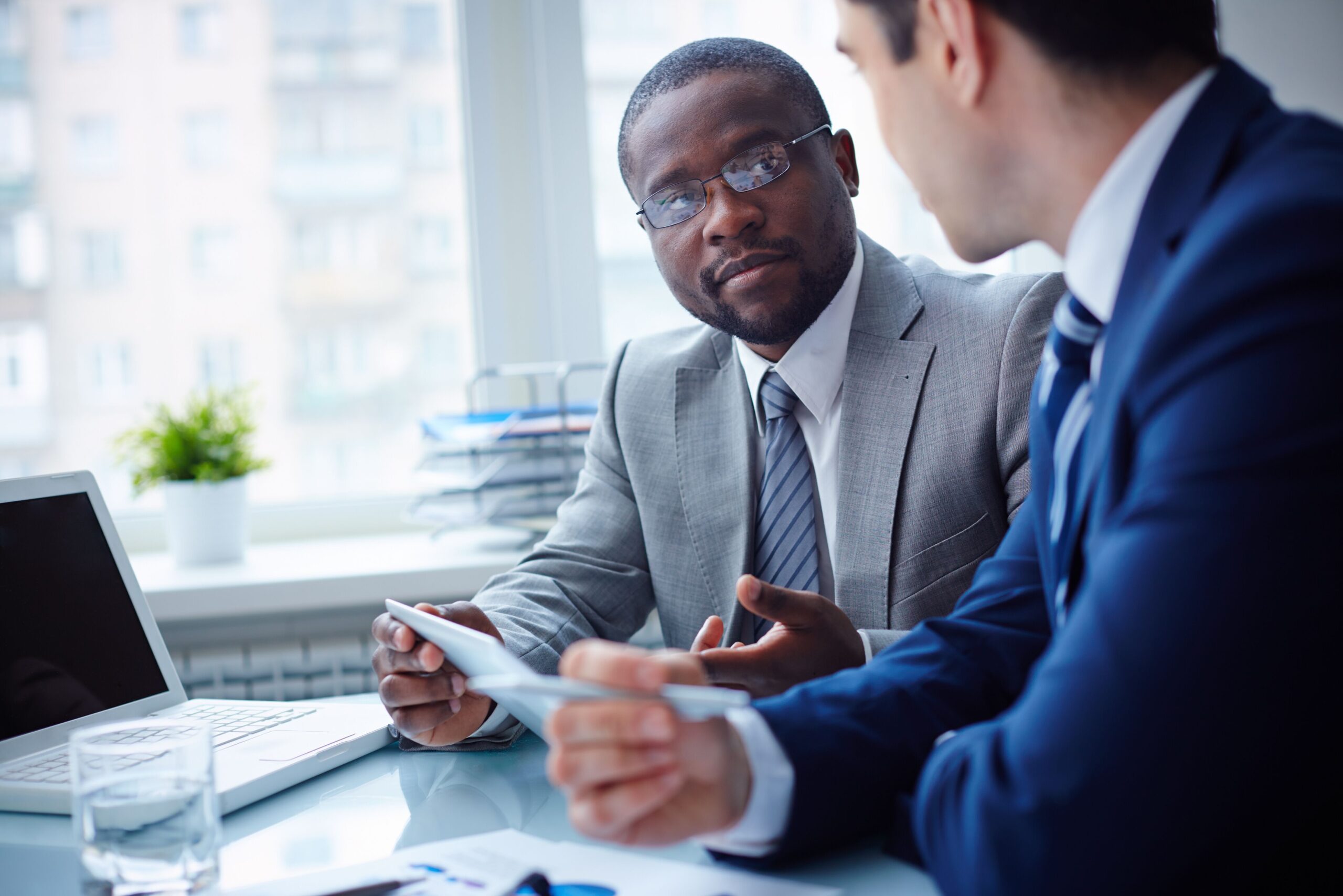 Two men in suits engage in a serious conversation at a bright office.